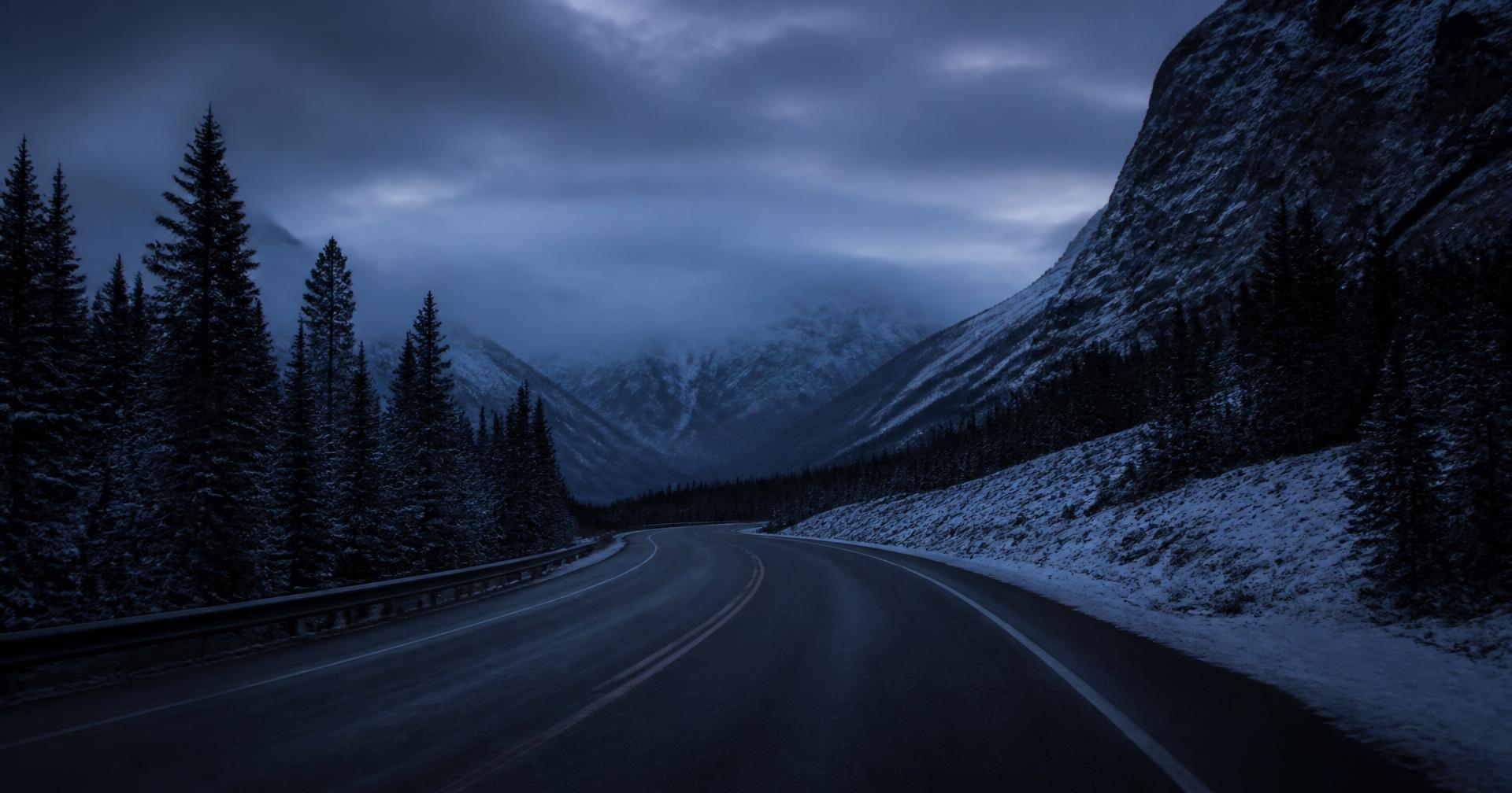 Footprints in thin snow along a dark stone trail below northern mountains at dusk